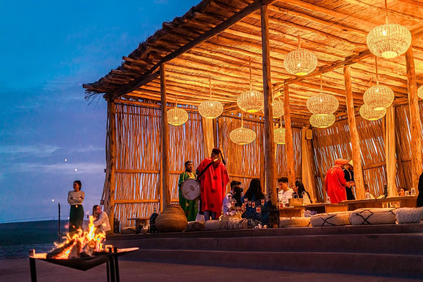 Soirée dîner-spectacle sous une paillote au crépuscule : tambour, lanternes et feu de camp