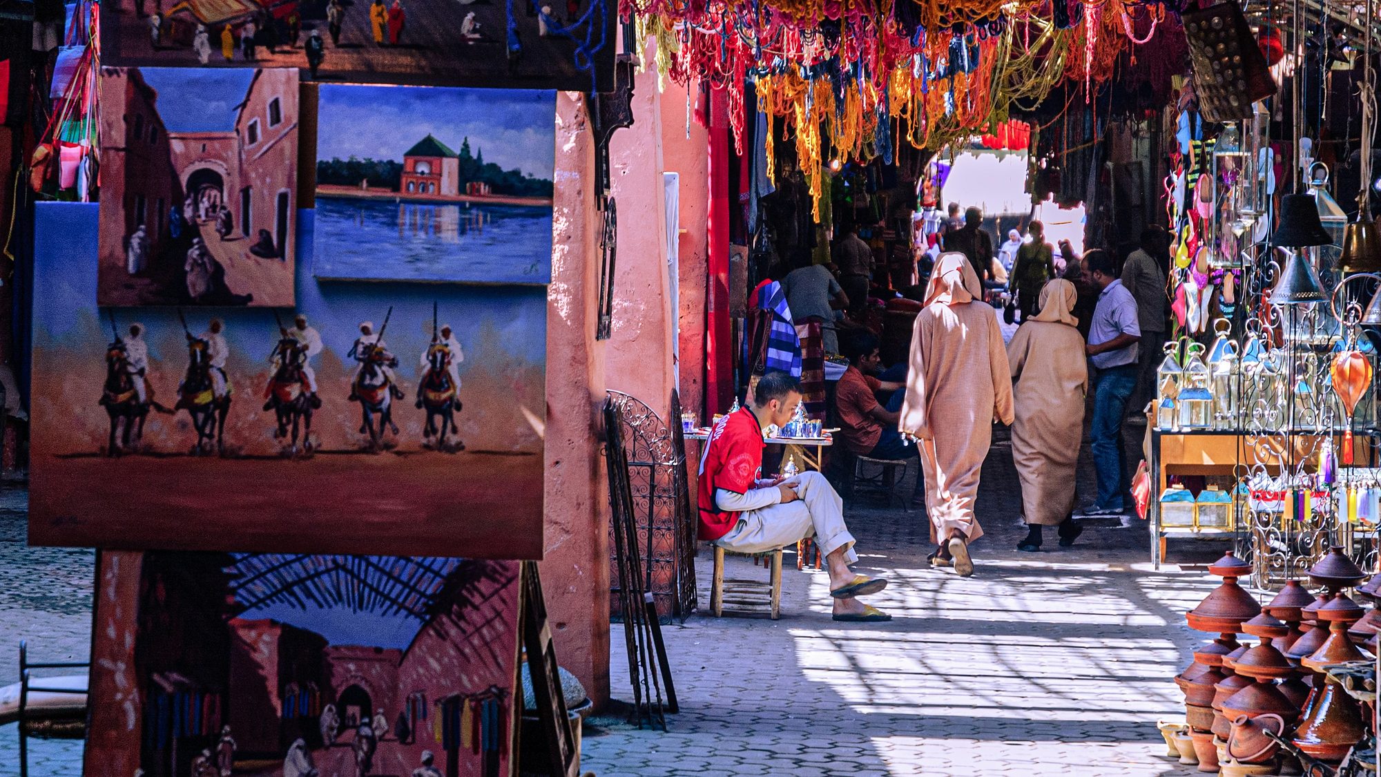 Ruelle animée du souk de Marrakech avec tableaux, laines colorées et poteries